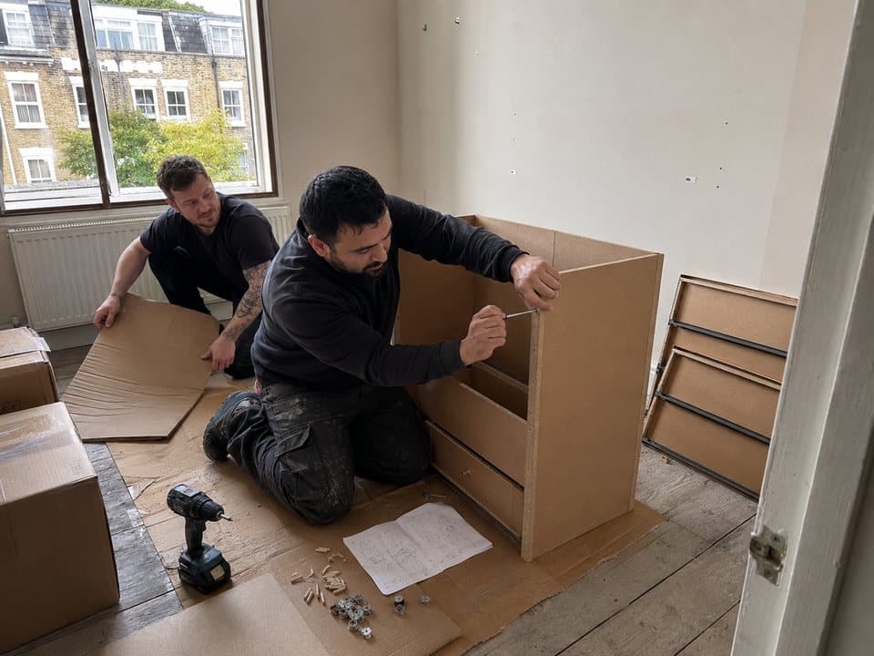 Furniture assembly in London: workers assembling a flat-pack chest of drawers on bare floorboards, with tools and fittings laid out