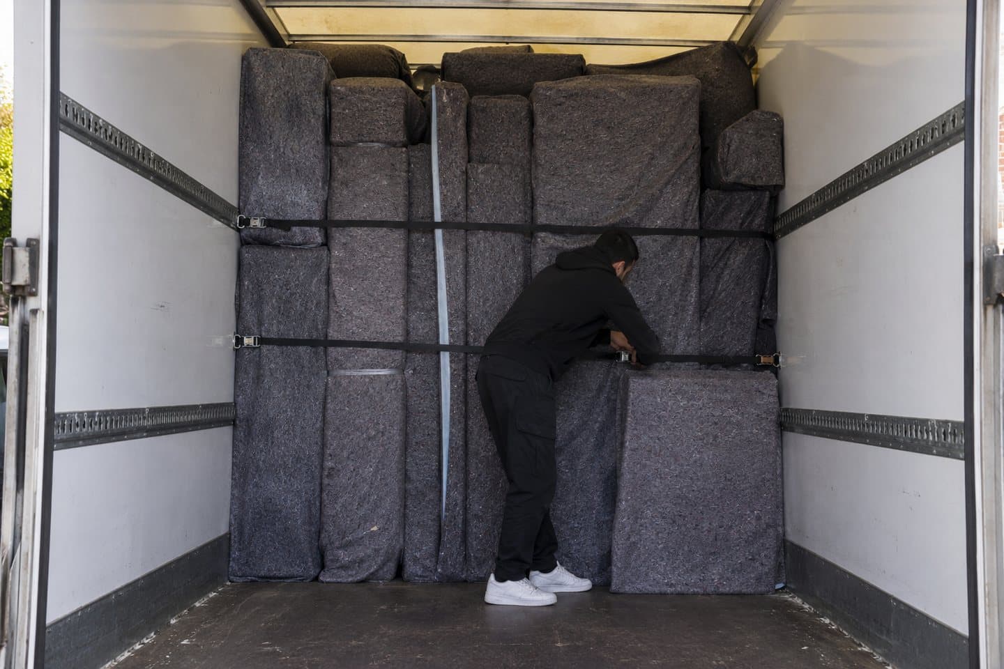 The inside of a fully loaded removals van, everything blanket-wrapped in tight rows and held with ratchet straps, a crew member checking the load.