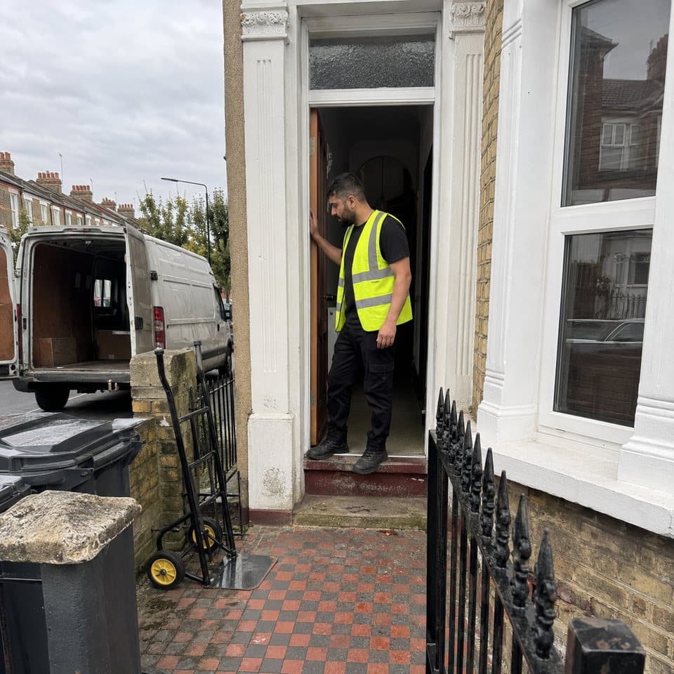 A crew member carrying a load through the front door of a London terrace.