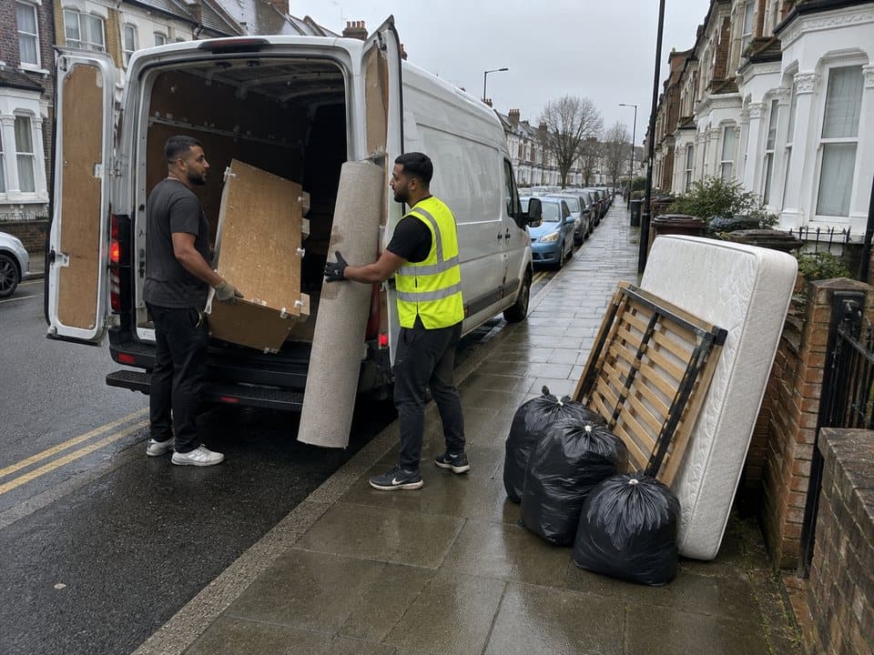Rubbish removal in London: Removal crew loading a mattress, a bedframe and tied sacks from the kerb into a van