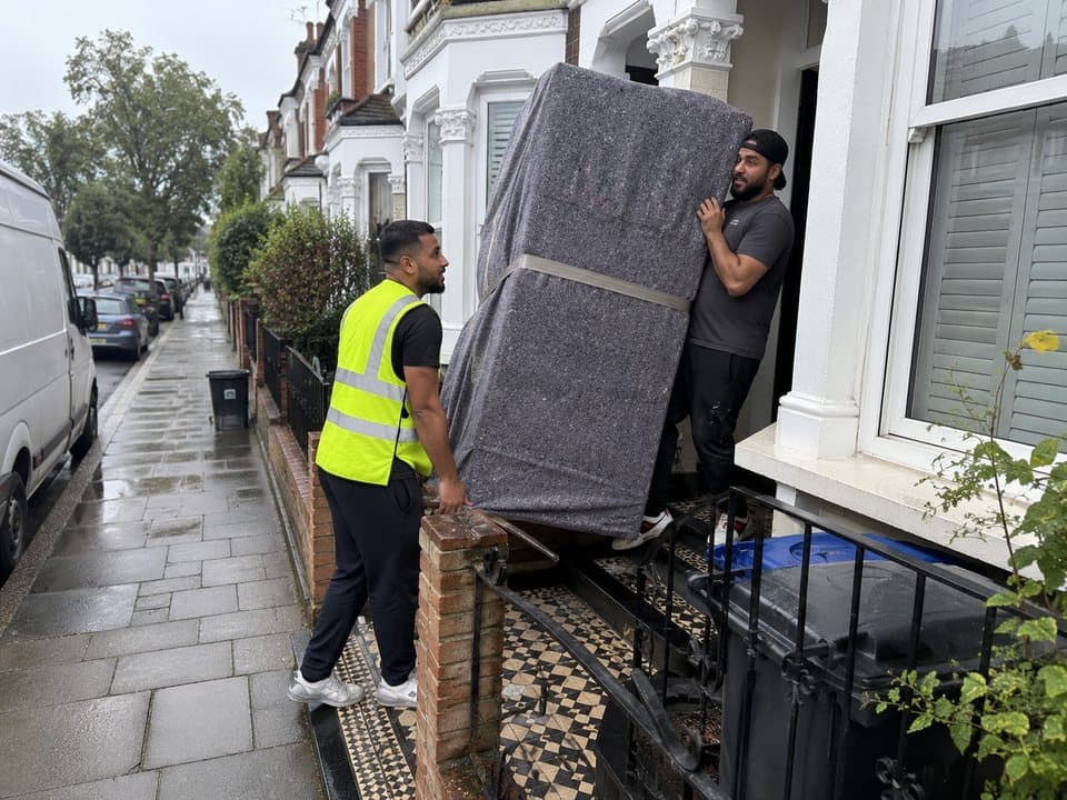 Furniture delivery in London: removal crew carrying a blanket-wrapped wardrobe up the front steps of a London terraced house