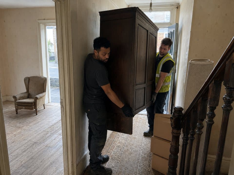 House clearance in London: removal crew easing a large old wardrobe down the hallway of a house being cleared